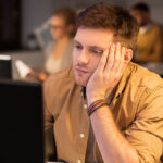 Mann med hodet i hendene foran PC. Foto.