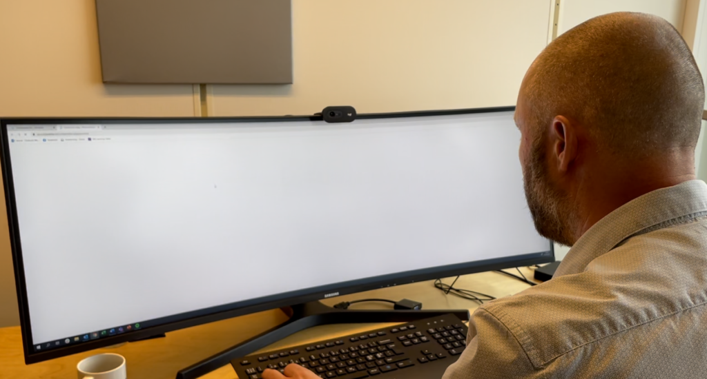 Foto: Mannsitter på kontor med stor PC-skjerm