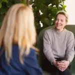 Foto: To damer sitter og snakker sammen i hver sin stol. Den ene sitter med ryggen til og den andre ser rett inn i kamera.