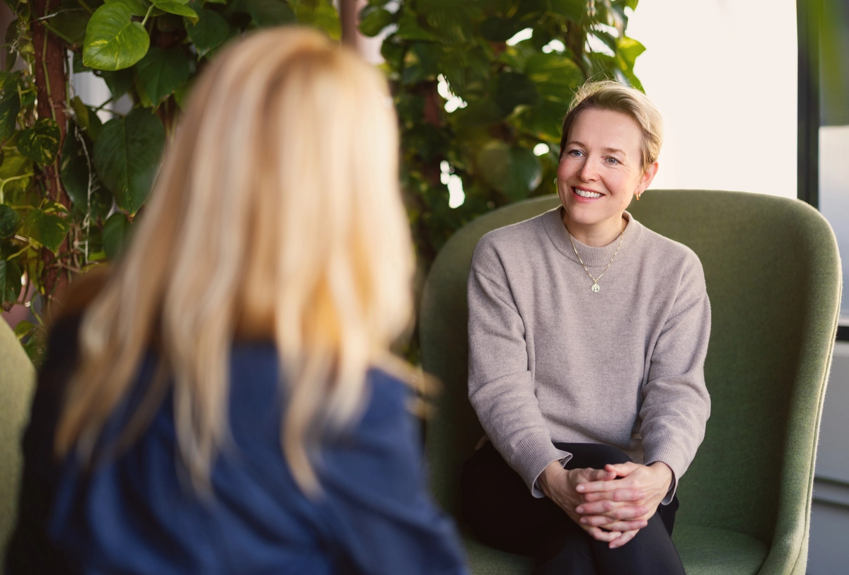 Foto: To damer sitter og snakker sammen i hver sin stol. Den ene sitter med ryggen til og den andre ser rett inn i kamera.