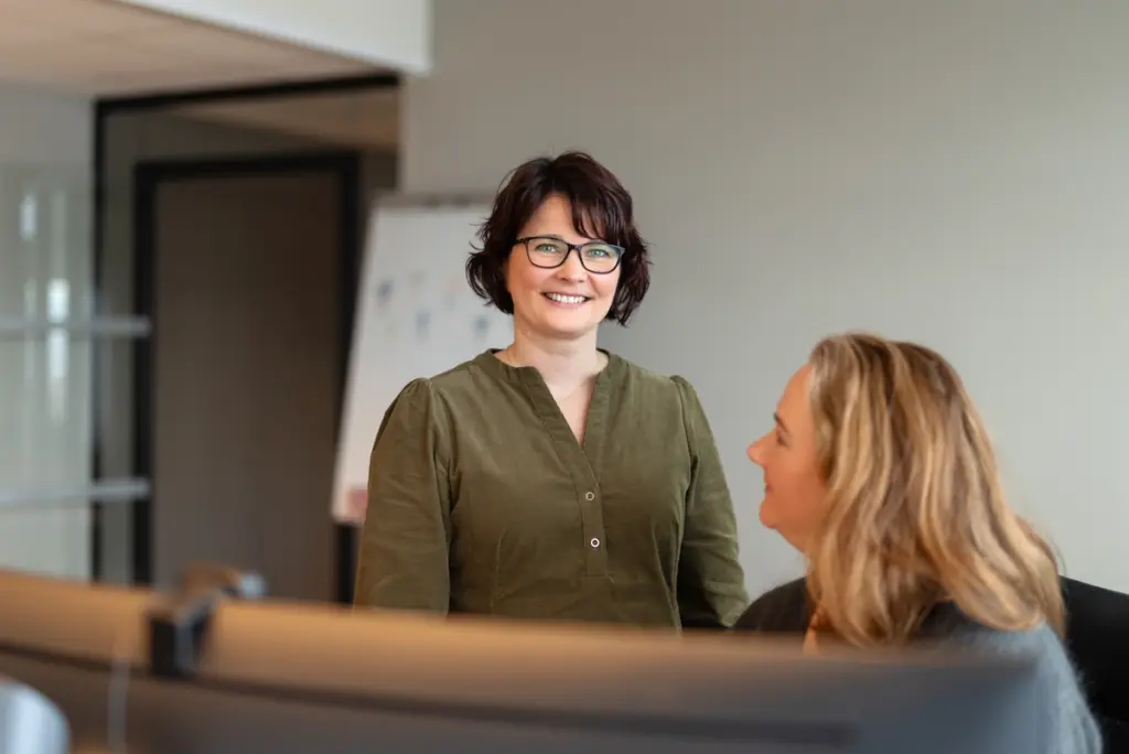 To damer som snakker sammen foren en stor krummet dataskjerm