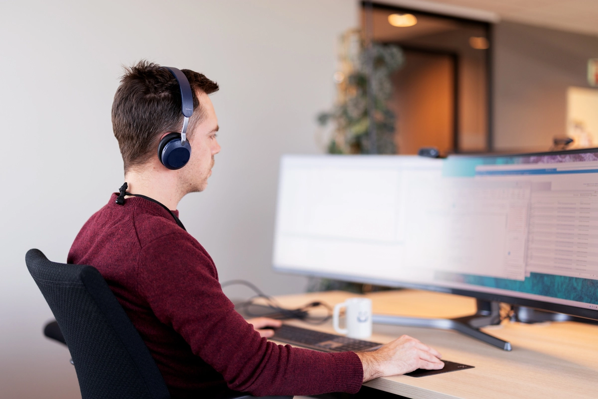 Mann som sitter med ryggen ved kontorpult og en stor skjerm,